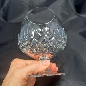 May include: A clear crystal brandy snifter featuring a wide, rounded bowl with a detailed diamond-cut pattern around the midsection. The glass has a short, sturdy stem and a circular base, showcasing intricate geometric facets that reflect light.