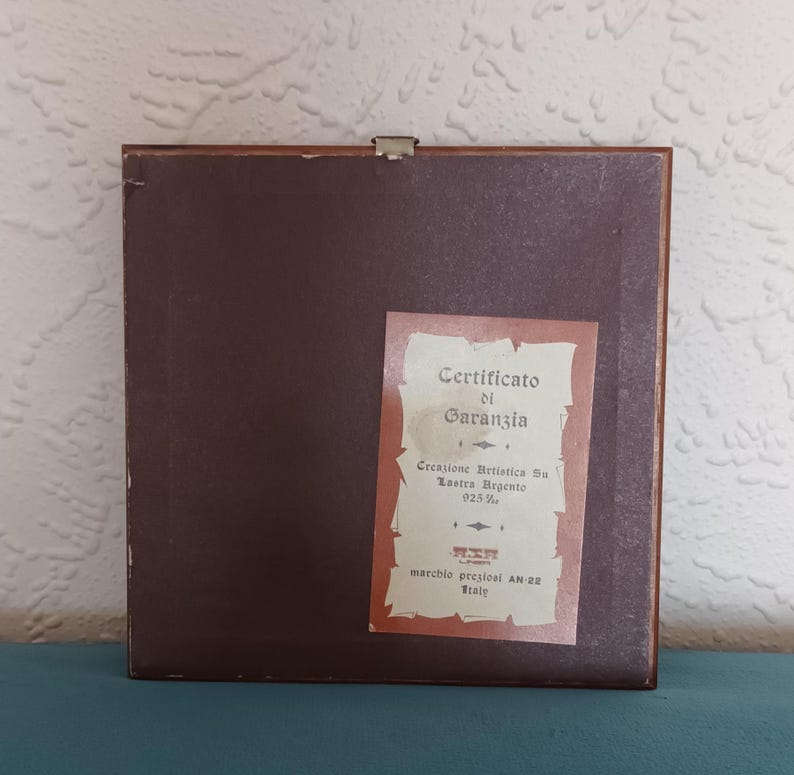 Puede incluir: Un marco de madera marr&oacute;n con un certificado de garant&iacute;a para una creaci&oacute;n de plata. El certificado dice "Certificato di Garanzia", "Creazione Artistica Su Lastra Argento 025%", "marchio preziosi AN-22 Italy".