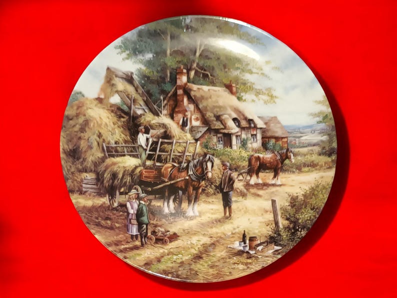 Pode incluir: Um prato de porcelana vintage com uma pintura de uma cena rural. A pintura representa uma carro&ccedil;a puxada por cavalos carregada de feno, dois cavalos, uma cabana com telhado de palha e v&aacute;rias figuras. A cena se passa em um campo com &aacute;rvores e uma vista distante de uma cidade.