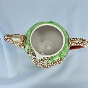 Pu&ograve; includere: Vista dall'alto di una teiera decorativa con un design verde, bianco e oro. La teiera ha un corpo rotondo, un beccuccio e un manico. Il manico e il beccuccio sono accentuati da dettagli dorati e bianchi. L'interno della teiera &egrave; bianco.