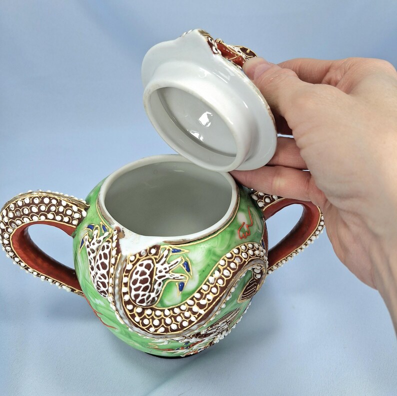 Pu&ograve; includere: Zuccheriera in ceramica con coperchio sollevato. La ciotola &egrave; verde con un disegno di drago marrone, bianco e oro. Le maniglie sono marroni con puntini bianchi. Il coperchio &egrave; bianco con un disegno marrone e rosso.