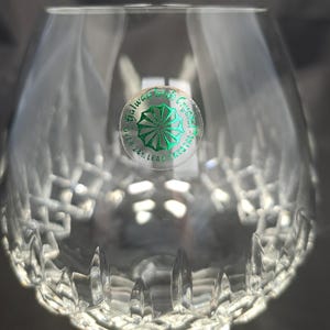 May include: A clear crystal brandy glass featuring a cut diamond pattern around the base and a circular green sticker on the side. The sticker displays the text Galway Irish Crystal and Over 24% Lead Crystal with a central starburst graphic.