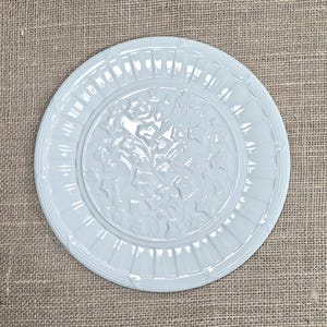K&ouml;nnte beinhalten: Eine runde, hellblaue Zierplatte mit einem erhabenen Blumendesign in der Mitte. Die Platte hat einen geriffelten Rand und ein detailliertes gepr&auml;gtes Muster. Die Platte ist aus Keramik gefertigt und eignet sich f&uuml;r dekorative Zwecke. Durchmesser ca. 25 cm.