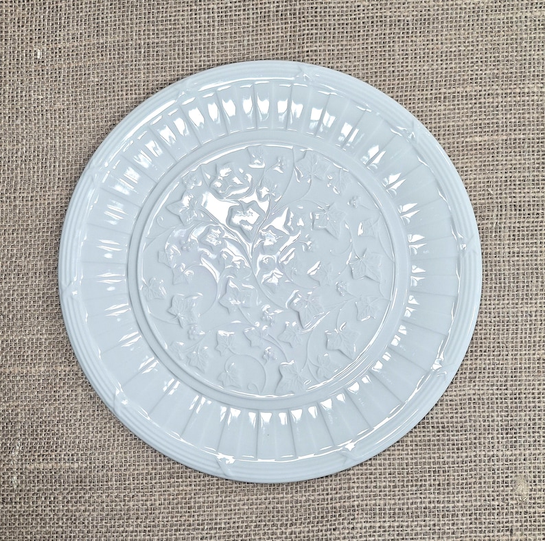 K&ouml;nnte beinhalten: Eine runde, hellblaue Zierplatte mit einem erhabenen Blumendesign in der Mitte. Die Platte hat einen geriffelten Rand und ein detailliertes gepr&auml;gtes Muster. Die Platte ist aus Keramik gefertigt und eignet sich f&uuml;r dekorative Zwecke. Durchmesser ca. 25 cm.