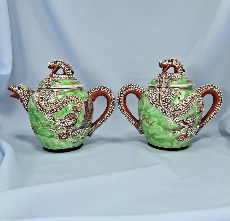 Pu&ograve; includere: Due teiere in ceramica verde abbinate con disegni di draghi. Le teiere hanno manici e beccucci marroni e i coperchi sono sormontati da figure di draghi. Le teiere sono decorate con accenti bianchi e marroni.