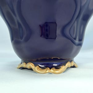 Może przedstawiać: Głęboko granatowe ceramiczne naczynie o gładkim, błyszczącym wykończeniu i zakrzywionej, falistej podstawie. Dolna krawędź naczynia jest podkreślona metalicznym złotym wykończeniem, kt&oacute;re podąża za falistym kształtem podstawy, tworząc kontrast.