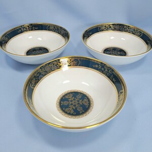 Op de afbeelding: Drie witte keramische kommen met een brede donkerblauwe rand met een goudkleurig bloemmotief en een bijpassend cirkelvormig goud en blauw bloemmotief in het midden. Elke kom heeft een dunne gouden rand aan de bovenkant en een gladde afwerking.