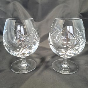 Puede incluir: Un par de copas de brandy de cristal transparente con un patr&oacute;n de corte profundo de estrella y rayado cruzado. Cada copa tiene un cuenco ancho y redondeado, un tallo corto y una base circular. El nombre Waterford est&aacute; grabado en la base.