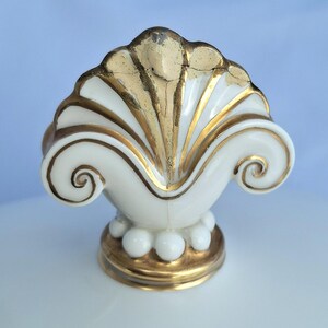 May include: A white and gold decorative shell-shaped object. The shell has a gold-painted top and accents, with a white base and a gold-trimmed bottom. The object has a detailed, ornate design.