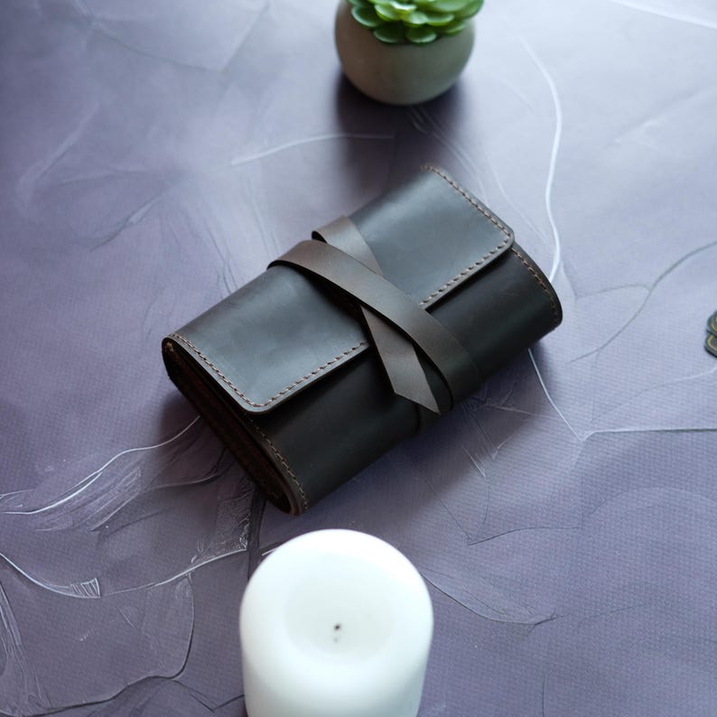 May include: A brown leather wallet with a strap closure. The wallet is folded and tied with a brown leather strap.