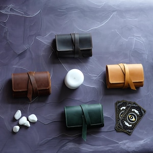May include: Four leather pouches in brown, black, tan, and green, with a white candle and a deck of tarot cards with an eye symbol on the front. The pouches have a strap closure.