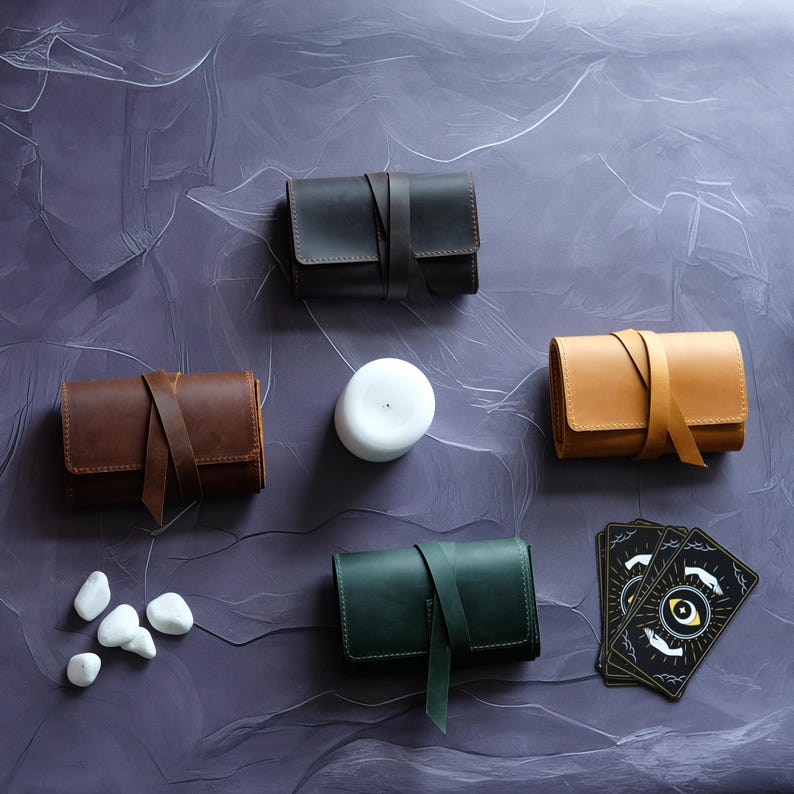 May include: Four leather pouches in brown, black, tan, and green, with a white candle and a deck of tarot cards with an eye symbol on the front. The pouches have a strap closure.
