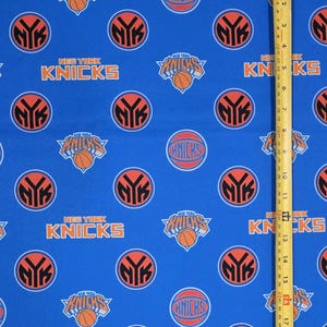 May include: Blue fabric featuring a repeating pattern of New York Knicks logos, basketball graphics, and the text New York Knicks. A yellow measuring tape is positioned vertically on the right side, showing a length of approximately 17 inches.