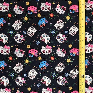 May include: Black fabric with a repeating pattern of white and pink sugar skull Hello Kitty characters with floral accents.