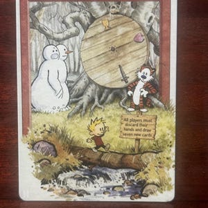 Puede incluir: Una carta de Magic: The Gathering titulada "Wheel of Fortune" con una ilustración caprichosa. La obra de arte representa una rueda de madera, un muñeco de nieve, un tigre y un niño cruzando un arroyo. La carta tiene un borde rojo y un coste de maná de dos.
