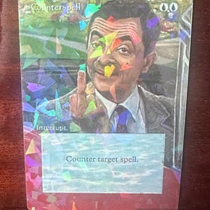 May include: A holographic trading card featuring a portrait of a man in a suit, giving the middle finger. The card reads "Counterspell" and "Interrupt" with the text "Counter target spell."