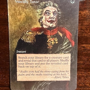 May include: A Magic: The Gathering card with a white background and a green mana symbol in the top right corner. The card is titled "Worldly Tutor" and features an illustration of a man with a sinister smile wearing a red and gold military uniform. The card text reads: "Instant. Search your library for a creature card and reveal that card to all players. Shuffle your library and put the revealed card back on top of it. "Aselbo soon had the rhino eating from his palm and the snake waiting at his heels." -Afari, Tales"