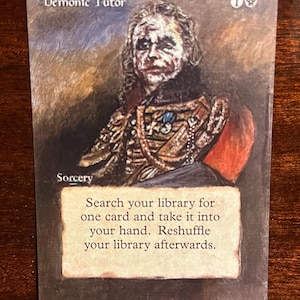Puede incluir: Una carta de Magic: The Gathering con un fondo oscuro y un retrato de un hombre con la cara blanca y el pelo oscuro. La carta se titula "Demonic Tutor" y tiene un coste de maná de 1 maná negro. El texto de la carta dice: "Busca en tu biblioteca una carta y ponla en tu mano. Baraja tu biblioteca después."