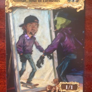 Puede incluir: Carta coleccionable con el texto "Animar, Soul of Elements". La carta muestra a una persona y un extraterrestre en un espejo. El extraterrestre lleva una sudadera con capucha morada y una gorra negra. Dos cachorros están en un monopatín. La carta tiene un borde dorado.