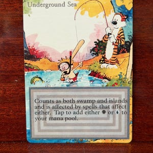 May include: A rectangular trading card titled Underground Sea featuring a cartoon illustration of a tiger and a child snorkeling in a blue river. The card includes text stating it counts as both swamp and islands and adds black or blue mana.