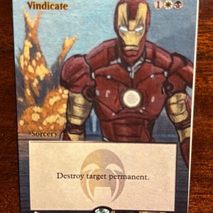 May include: A collectible card featuring Iron Man in a red and gold suit. The card has the word "Vindicate" at the top and the text "Destroy target permanent" at the bottom. The card is a sorcery.
