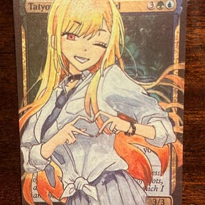 May include: A Magic: The Gathering card featuring a cartoon illustration of a woman with long blonde hair wearing a white shirt, a black tie, and a black skirt. The card is titled "Tatyo, the  d" and has a mana cost of 3 green and 1 blue. The card has a power and toughness of 3/3.