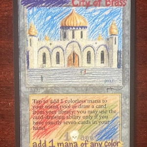 May include: A rectangular trading card titled City of Brass featuring a hand-drawn illustration of a white palace with a gold dome. The card includes text describing game mechanics, with colorful crayon scribbles overlaying the text box area.