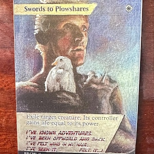 Op de afbeelding: Verzamelkaart "Swords to Plowshares" met een geschilderde illustratie van een persoon en een vogel. De kaart bevat tekst die de functie beschrijft en smaaktekst. De kaart komt uit de "DMR"-set.