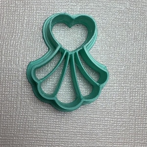 May include: A green plastic cookie cutter shaped like a seashell with a heart cutout at the top.
