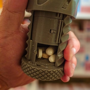 Puede incluir: Un pastillero de plástico gris con un compartimento para guardar varias pastillas. El pastillero tiene un diseño texturizado y un pequeño pestillo para abrir y cerrar los compartimentos.