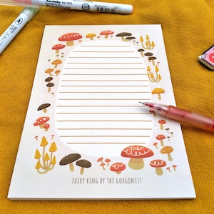 May include: A white notepad with a mushroom border. The notepad has lined paper and the text "Fairy Ring by the Gorgonist" at the bottom.