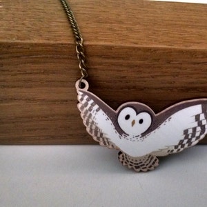 May include: A white and brown owl pendant necklace with a bronze chain. The owl is flying with its wings spread out.