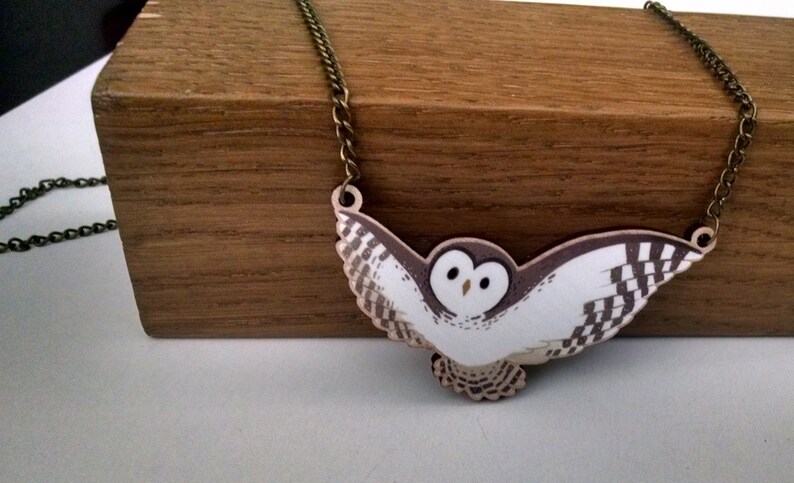 May include: A white and brown owl pendant necklace with a bronze chain. The owl is flying with its wings spread out.