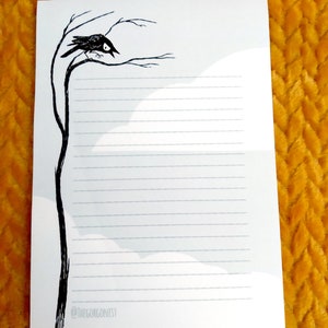 May include: A white lined paper notepad with a black and white illustration of a crow perched on a bare branch. The text "@thegorgonist" is at the bottom of the page.