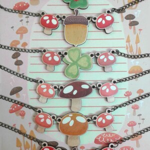 May include: Six necklaces with wooden charms featuring mushrooms, acorns, clovers, and butterflies. The charms are painted in various colors, including red, green, brown, and white. The necklaces are made with a brown chain.