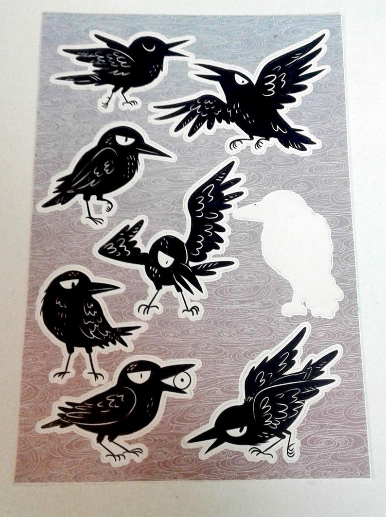 Pu&ograve; includere: Foglio di adesivi con illustrazioni di corvi neri stilizzati in varie pose. I corvi hanno occhi espressivi e sono raffigurati con becchi aperti e ali spiegate. Lo sfondo &egrave; grigio chiaro con un sottile motivo acquatico.