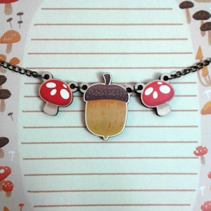 May include: A necklace with a brown acorn charm and two red and white mushroom charms. The necklace is made of a brown chain.