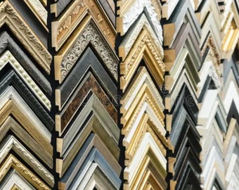 Puede incluir: Una colección de diversas molduras para marcos de fotos dispuestas en filas verticales. Las muestras presentan acabados variados que incluyen oro metálico, plata, bronce, negro mate, blanco y texturas de vetas de madera.