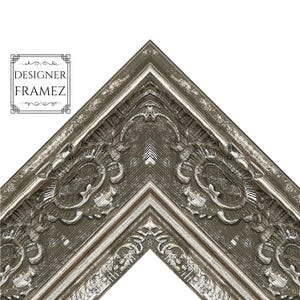 May include: Corner of a decorative picture frame with ornate carvings and a distressed silver finish. The frame has a dark gray base with lighter silver accents and the text "DESIGNER FRAMEZ".