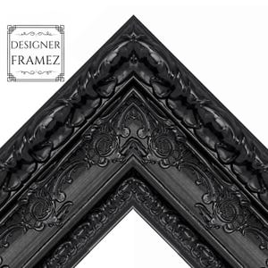 May include: Close-up of a corner of a black picture frame with ornate detailing. The frame has a glossy finish and features floral and scrollwork designs. The text "DESIGNER FRAMEZ" is in the upper left corner.