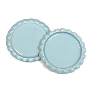 Puede incluir: Dos tapas de botella de metal azul claro con borde festoneado.