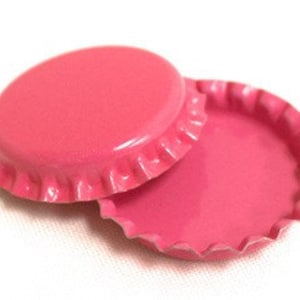 May include: Two pink bottle caps, one with the top side facing up and the other with the bottom side facing up.