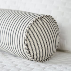 May include: A black and white striped bolster pillow with a rounded end. The pillow is made of a soft, woven fabric.