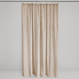 full length shot of a brown and cream ticking stripe fabric shower curtain hanging on a shower curtain rod against a neutral background