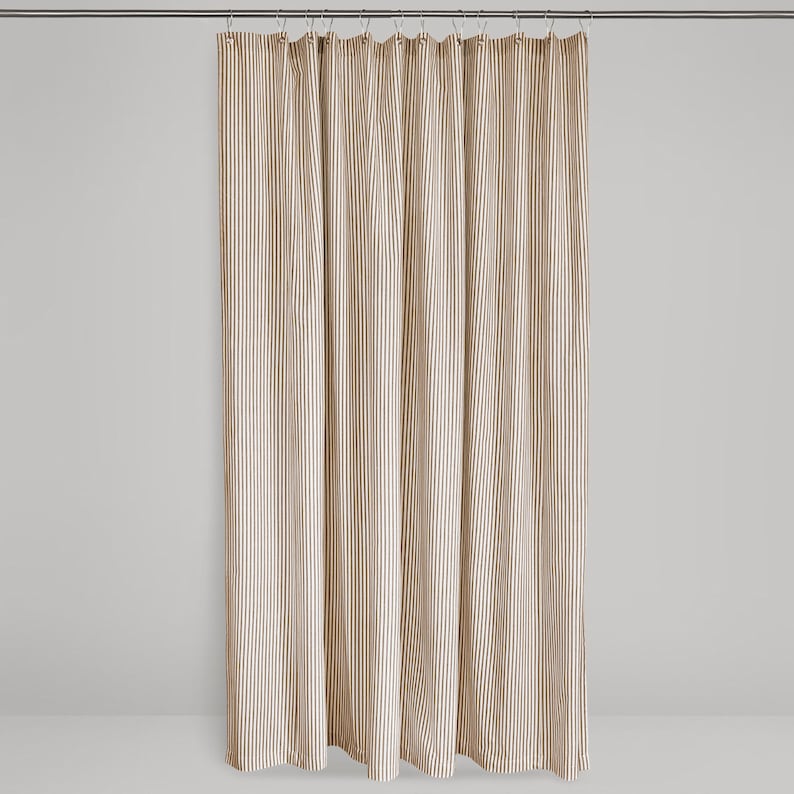 full length shot of a brown and cream ticking stripe fabric shower curtain hanging on a shower curtain rod against a neutral background