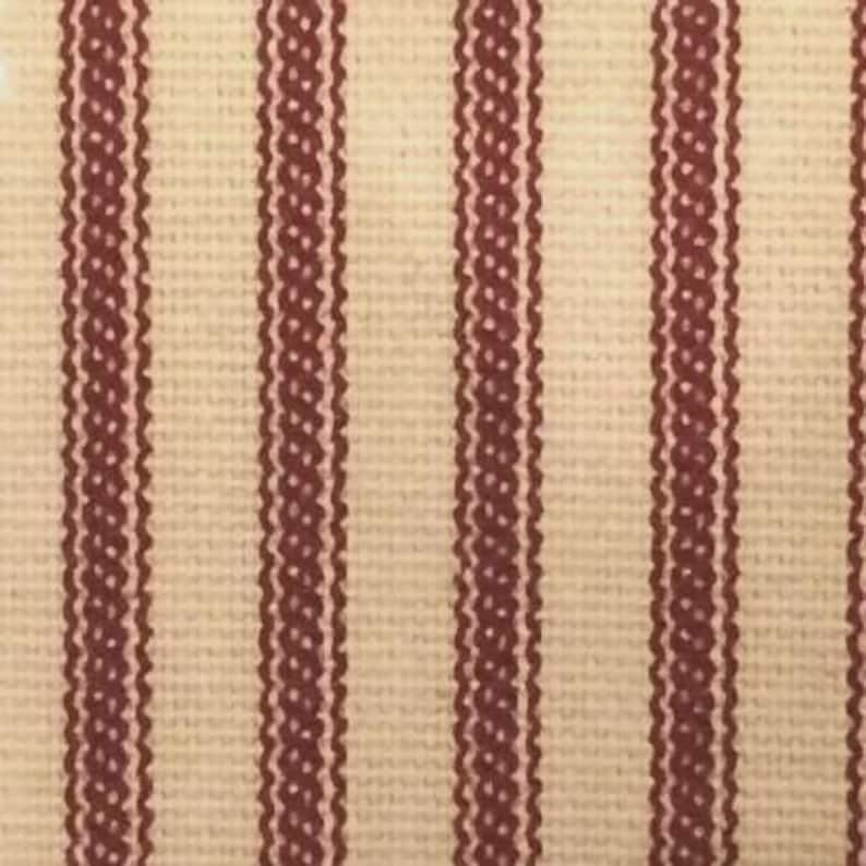 Puede incluir: Una tela tejida con un patr&oacute;n repetitivo de rayas verticales. El dise&ntilde;o consiste en bandas anchas de color crema que se alternan con rayas m&aacute;s estrechas de color granate oscuro, con un borde decorativo ondulado y texturizado.