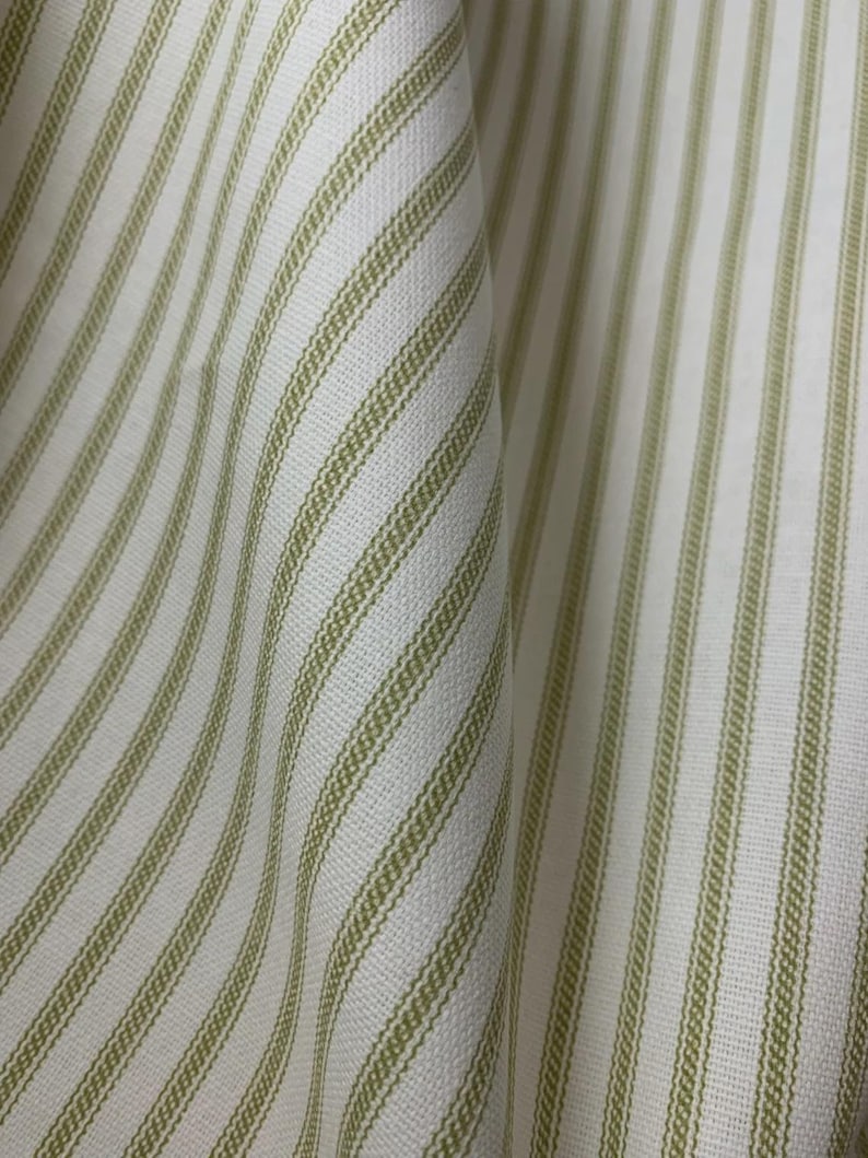 Puede incluir: Una tela tejida con un patr&oacute;n repetitivo de rayas verticales de color verde salvia sobre un fondo blanco. El material muestra una textura de tejido visible con pliegues suaves que crean profundidad y dimensi&oacute;n en toda la superficie.