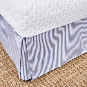 May include: A white bed skirt with blue and white stripes. The skirt is pleated and has a simple design.