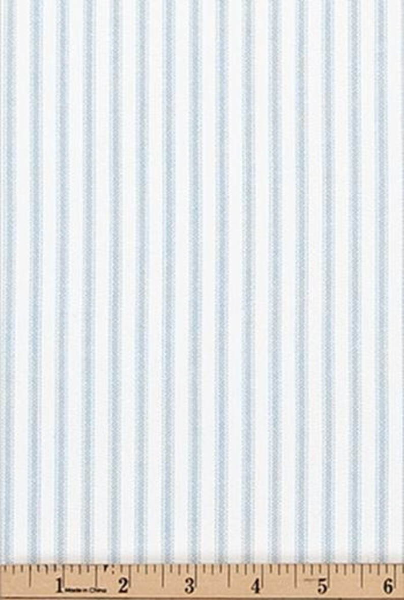 Puede incluir: Una tela blanca con un patr&oacute;n repetitivo de rayas verticales de color azul claro. Una cinta m&eacute;trica est&aacute; colocada en el borde inferior, mostrando una escala de 15 cent&iacute;metros, indicando la escala del patr&oacute;n de la tela y el ancho del material.