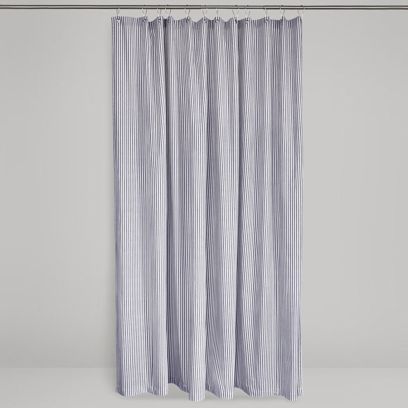 full length shot of a fabric shower curtain in blue and cream ticking stripe fabric hanging on a shower curtain rod  against a plain background